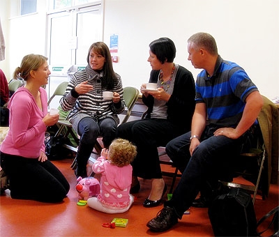 Four adults talking while a toddler sits on the floor playing in front of them