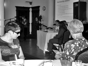 People at tables watching a speaker at a podium and others seated as a panel