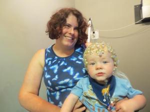 Beth with baby on her lap who is wearing a net of electrodes on his head
