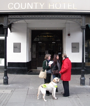 Three woman and a guide dog outside the entrance to The County Hotel