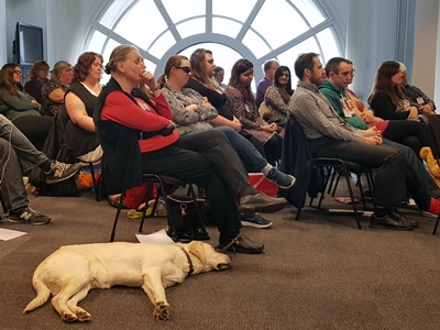 Seated audience and a guide dog laying on the floor