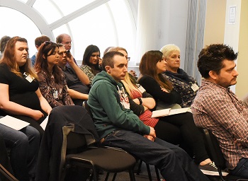 Different kinds of people sitting in rows of seats, one using a monocular