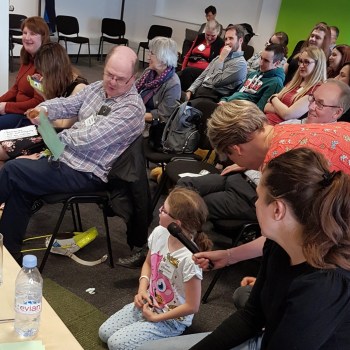 Seated delegates. Woman holding microphone for child knelling on the floor