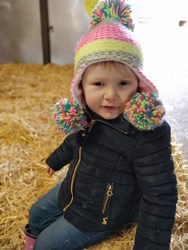 Rhiannon wearing a wooly hat with large colourful bobbles by each ear and on the top.