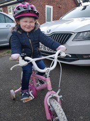 Rhiannon smiling as she rides a pink bike.