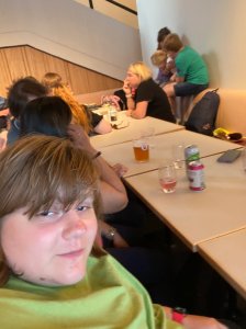 Selfie of Amy at cafe table with other adults and children in the background