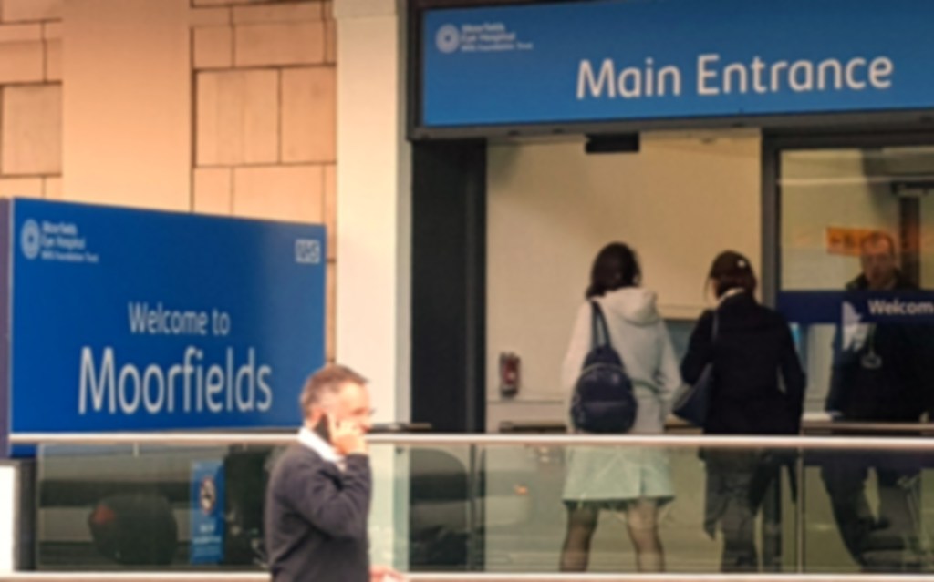 Slightly blurry photo of the front of Moorfields Eye Hospital. Text can be read and people's features seen. No black edge of a bubble.